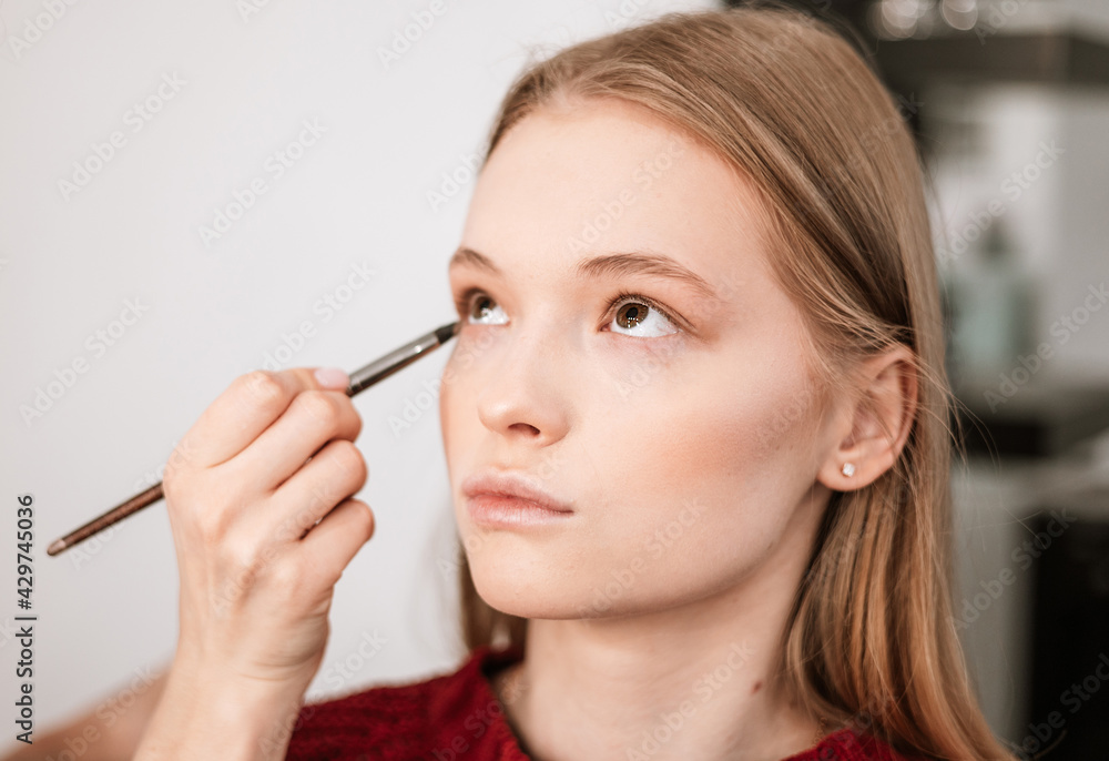 makeup artist applies eye shadow to the eyelids on a beautiful young woman blonde model, face make up concept makeup artist applies eye shadow to the eyelids on a beautiful young woman blonde model, face make up concept