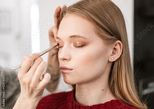 makeup artist applies eye shadow to the eyelids on a beautiful young woman blonde model, face make up concept