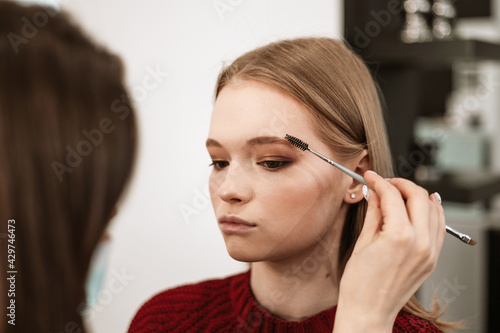 makeup artist applies eyebrow shadow on a beautiful young woman blonde model  face make up concept