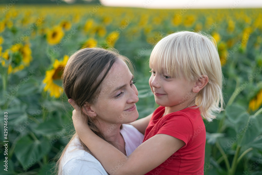 Cute blond boy hugs his mom. Love and trust. Blooming sunflowers field on background Cute blond boy hugs his mom. Love and trust. Blooming sunflowers field on background