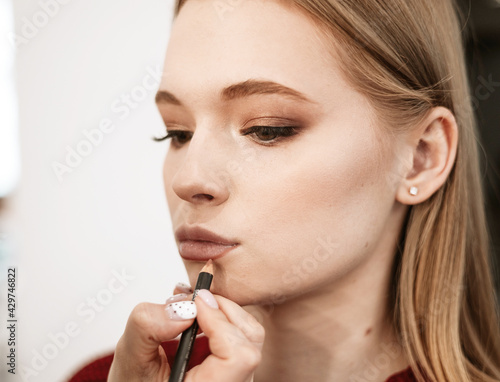 makeup artist paints lips with lipstick with a brush on a beautiful young woman blonde model, face make up concept