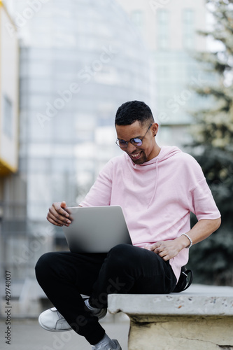 Handsome young man in glasses working on laptop outdoors on a background of corporate building