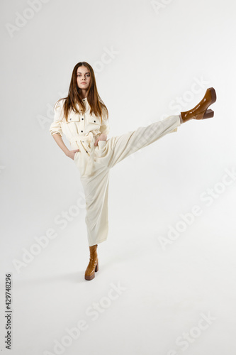 beautiful woman in white jumpsuit with raised leg up on isolated background