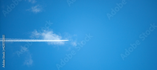 A plane flies through a white cloud in a blue sky