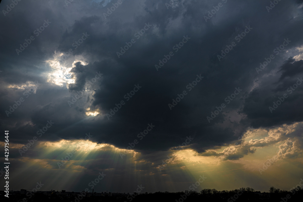 Dark sky with clouds, through which the rays of the sun break through