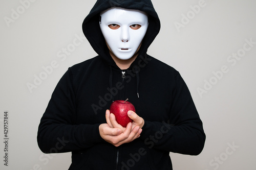 Hacker with anonymous mask holding an apple with his both hands