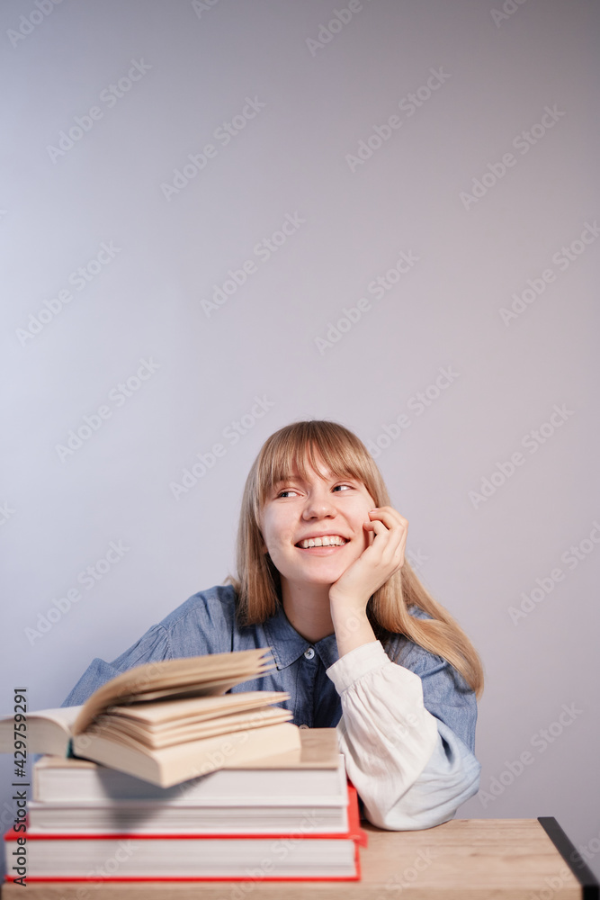 Happy blonde student girl with bunch of books relaxing. Young beautiful caucasian pupil female with books in class with copy space. Back to school or homeschooling concept. High quality vertical photo Happy blonde student girl with bunch of books relaxing. Young beautiful caucasian pupil female with books in class with copy space. Back to school or homeschooling concept. High quality vertical photo