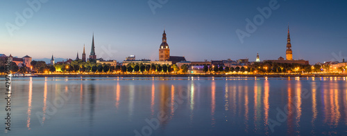 Panoramic view of old Riga town at night with church towers and castle reflections of light in river