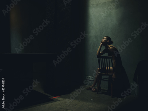 woman sitting on a chair in a dark room falling light loneliness emotions upset depression
