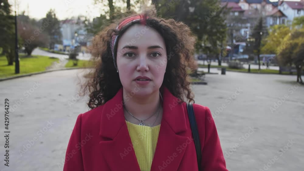 Young beautiful curly woman in a red coat goes and puts on a mask Young beautiful curly woman in a red coat goes and puts on a mask