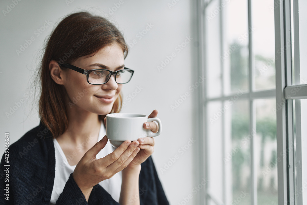 woman with glasses at home near the window with a cup of coffee rest woman with glasses at home near the window with a cup of coffee rest