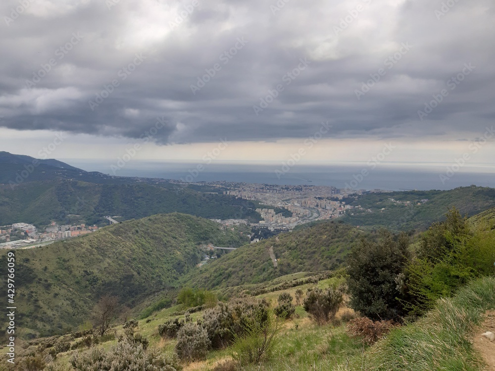 Discovering the mountains around Genoa. Panoramic view to the city. Grey sky in the background. First green leaves in spring.