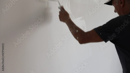 Painter man painting a blank wall, with paint stick roller in empty white room with copy space. Vertical Shot. photo