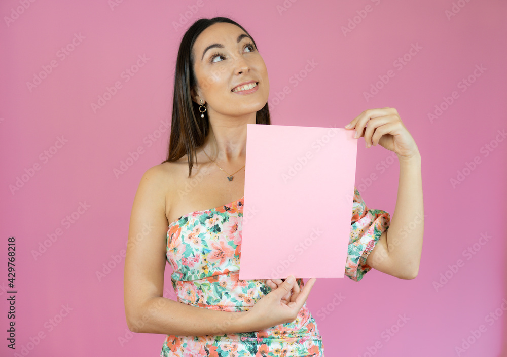 Young beautiful woman smiling and holding a blank sheet of paper isolated over pink background. Young beautiful woman smiling and holding a blank sheet of paper isolated over pink background.