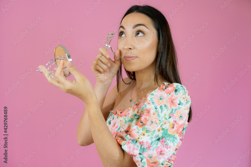 Young woman curling her eyelashes looking in a pocket mirror Young woman curling her eyelashes looking in a pocket mirror