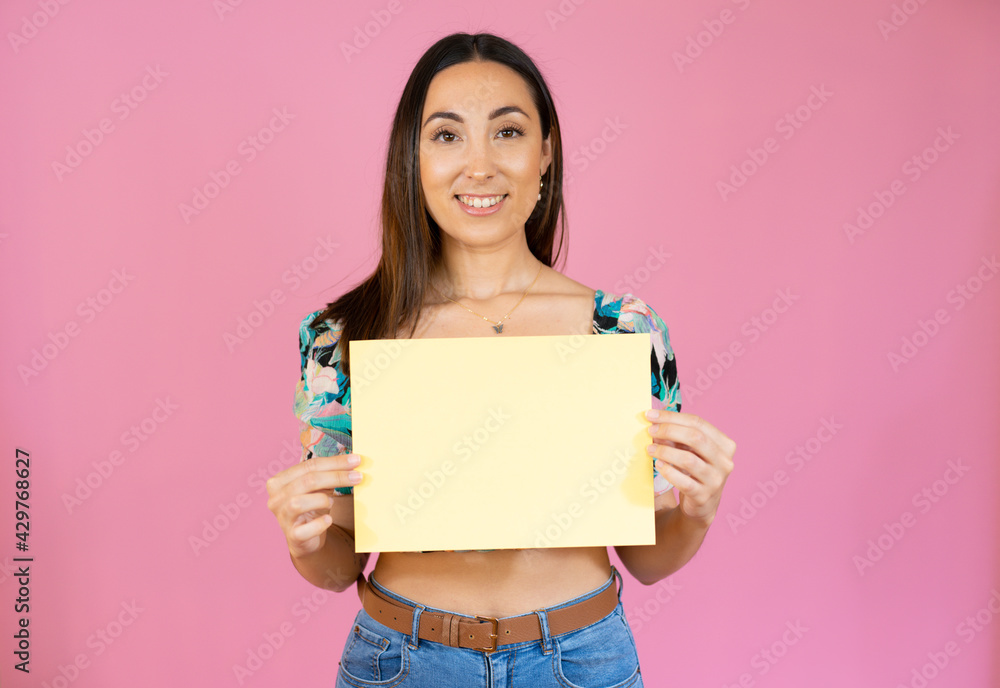Young beautiful woman smiling and holding a blank sheet of paper isolated over pink background. Young beautiful woman smiling and holding a blank sheet of paper isolated over pink background.
