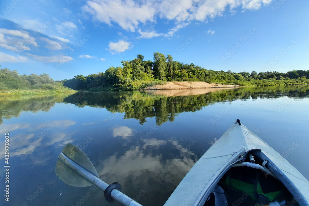 The blue bow of the kayak and the paddle on the background of the vast surface of the lake. The sky is beautifully reflected on the water. Water sports in nature. Concept: adventure, sports, fun