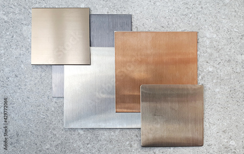 multi colored of hairline aluminium plate samples containg gold ,silver ,nickle silver ,copper ,black colors placed on grey stone tile. top view of interior metallic plate samples. mood tone board. photo