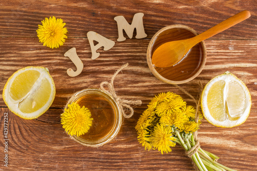 Homemade delicious dandelion jam on a wooden table with yellow dandelions. Dandelion flower syrup. Useful preservation for the winter