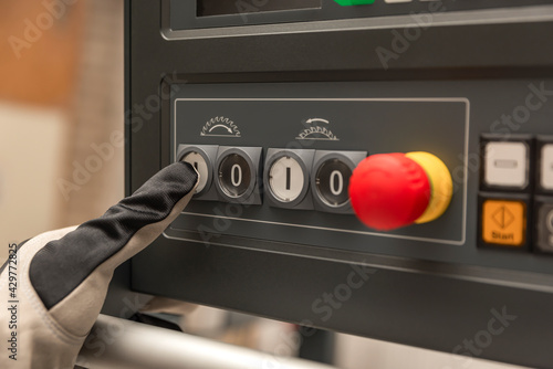 Hand presses the power button of a woodworking machine at a factory.