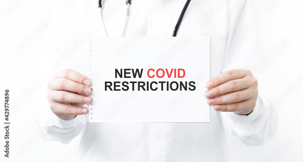 text new covid restrictions on a notepad in the hands of a doctor on a white background, medical concept. text new covid restrictions on a notepad in the hands of a doctor on a white background, medical concept.