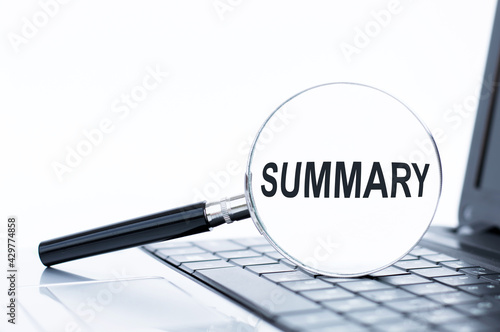 The word Summary on magnifying glass, which is on the laptop keyboard. Business concept.