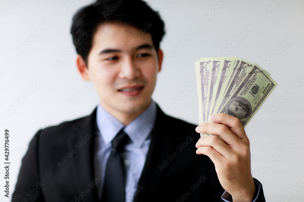 Selective focus on holding dollar bank notes or money with blur background of asian smiley business man. Financial Concept. Selective focus on holding dollar bank notes or money with blur background of asian smiley business man. Financial Concept.