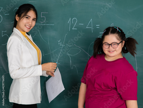 Down syndrome young girl widely smiles with pride and a happy face when she can answer the correct numbers on green board in classroom. Concept for education and studying of disabling kid in school.