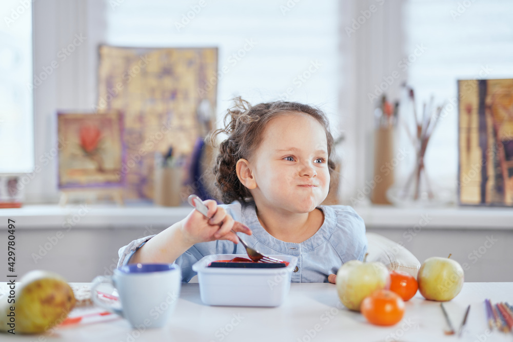Funny laughing girl is having dinner sitting at the table stuffed mouth with food. Small cute schoolgirl having lunch. Eating using fork from lunch box. Tasty eating concept. High quality image