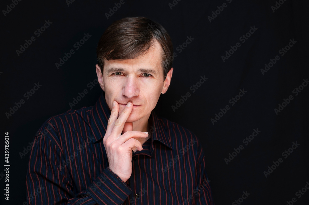 Middle-aged man with a pensive serious face on a dark background. Dramatic portrait of a middle-aged man in a shirt, he decides what to do Middle-aged man with a pensive serious face on a dark background. Dramatic portrait of a middle-aged man in a shirt, he decides what to do