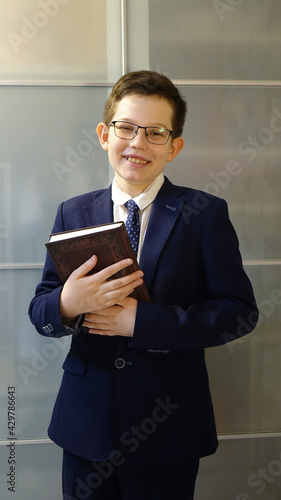 School boy in eyegasses is holding a book and laugh. photo