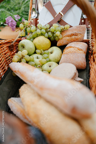 Fresh fruits, green apples, grapes and crispy wheat bread for a family picnic in nature. Wicker basket with products for a healthy family breakfast on the lawn.