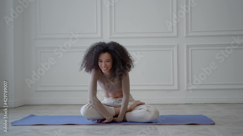 Young african woman on a blue sports mat in white living room, hard to do sport exercises. Non-athletic, unsporting beautiful woman falling while doing exercises