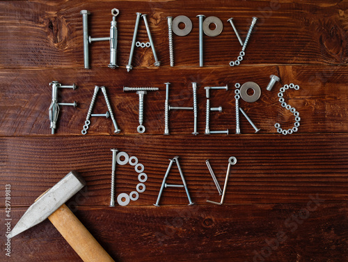 Text Happy Father's day made from metallic bolts and iron nails with hammer on wooden background. Greeting card. Creative congrats concept for dad's day celebration.