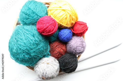Top view of multicolored yarn in basket and knitting needles on white background 