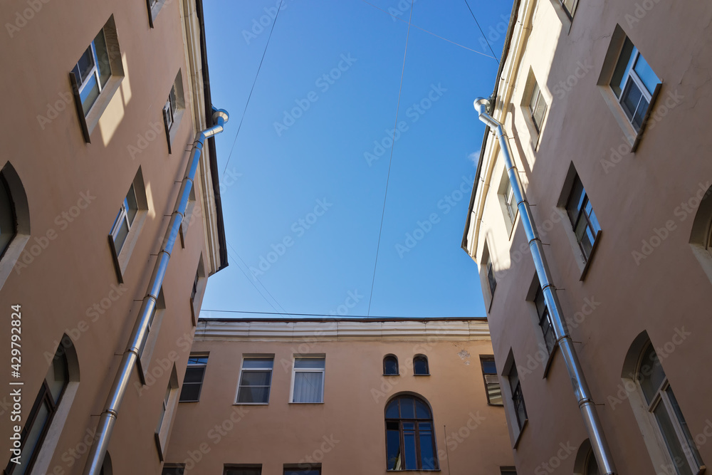 Bottom view of the courtyard-well typical for old St. Petersburg at background of the blue sky. Houses are built close to form a small patio