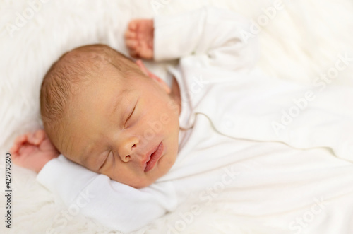 Adorable newborn one week age in white bedroom. Newborn child relaxing in bed. Nursery for young children. Textile and bedding for kids. Family morning at home. Lifestyle concept, real life.