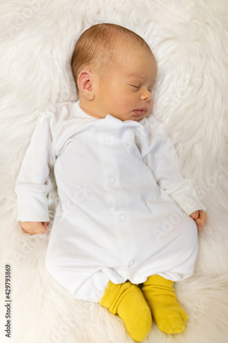 Adorable newborn one week age in white bedroom. Newborn child relaxing in bed. Nursery for young children. Textile and bedding for kids. Family morning at home. Lifestyle concept, real life.
