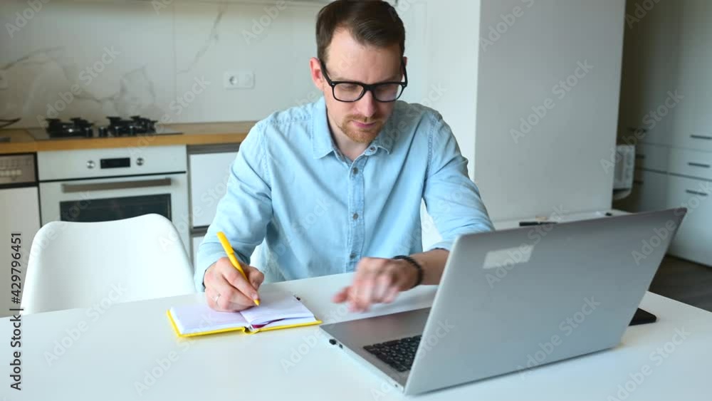Focused male entrepreneur takes notes using a laptop for remote work from home, concentrated ambitious man watching training courses or webinar, studying online and writing down Focused male entrepreneur takes notes using a laptop for remote work from home, concentrated ambitious man watching training courses or webinar, studying online and writing down