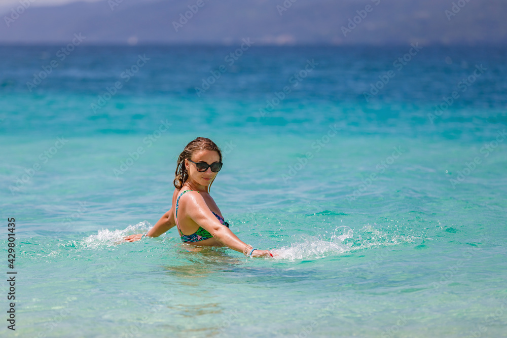 Young beautiful girl splashes in the blue water of the ocean.