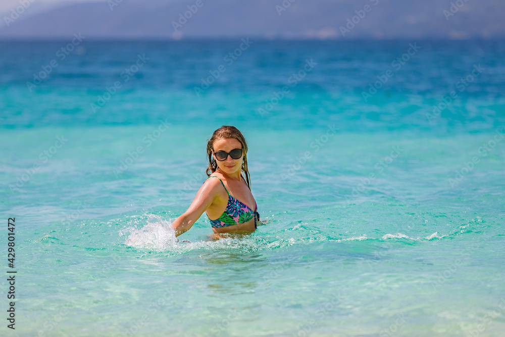 Young beautiful girl splashes in the blue water of the ocean.