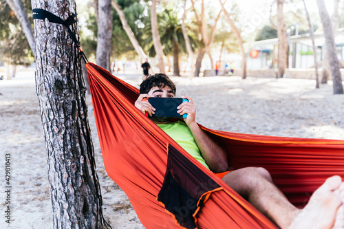 Caucasian man lying in a hammock and playing video games at Palmanova beach. Palma de Mallorca, Spain (Perfect for Copyspace)