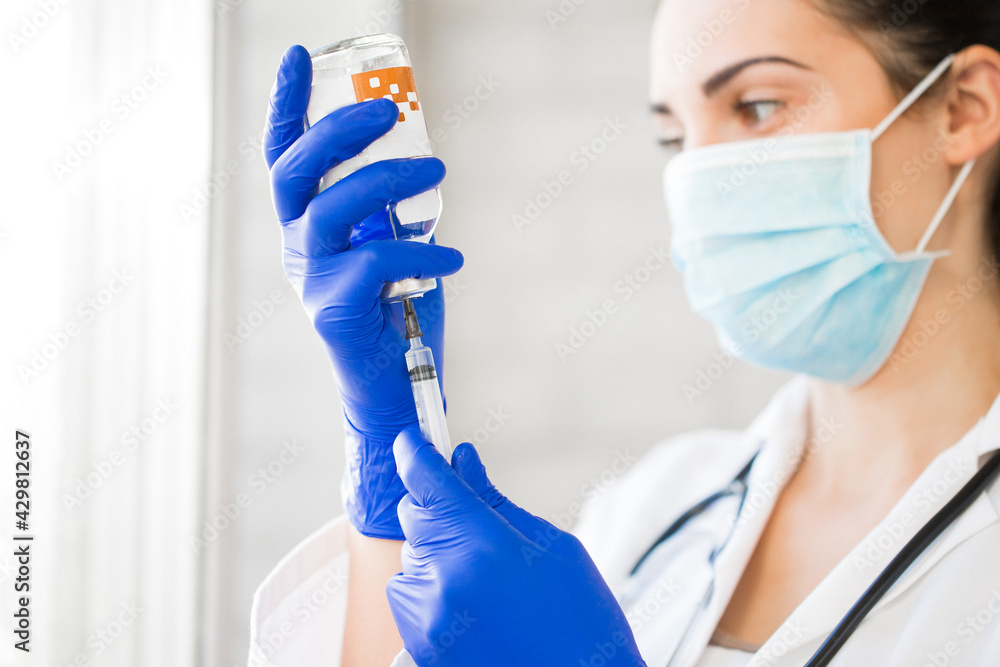 Side view of the young doctor who is dialing a medicine into a syringe indoors Side view of the young doctor who is dialing a medicine into a syringe indoors