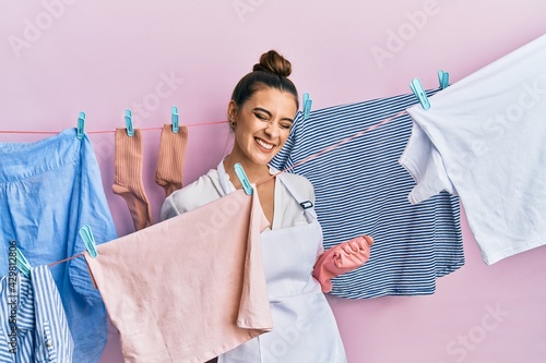 Beautiful brunette young woman washing clothes at clothesline excited for success with arms raised and eyes closed celebrating victory smiling. winner concept.