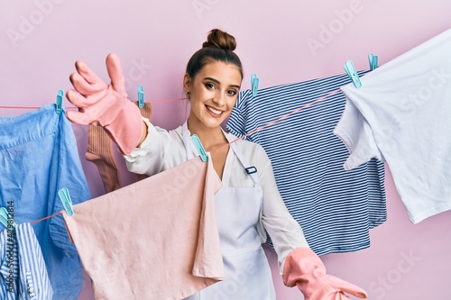 Beautiful brunette young woman washing clothes at clothesline looking at the camera smiling with open arms for hug. cheerful expression embracing happiness.