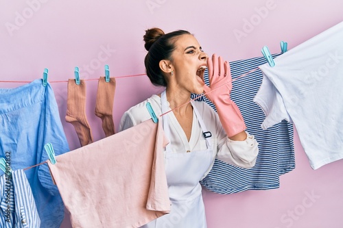 Beautiful brunette young woman washing clothes at clothesline shouting and screaming loud to side with hand on mouth. communication concept.