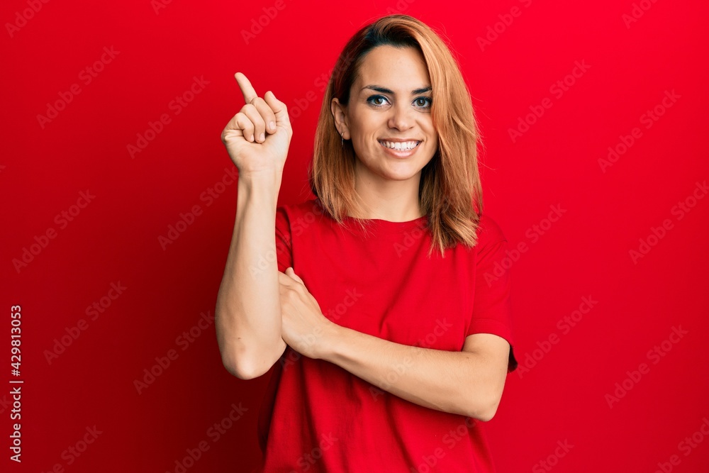 Hispanic young woman wearing casual red t shirt with a big smile on face, pointing with hand and finger to the side looking at the camera. Hispanic young woman wearing casual red t shirt with a big smile on face, pointing with hand and finger to the side looking at the camera.