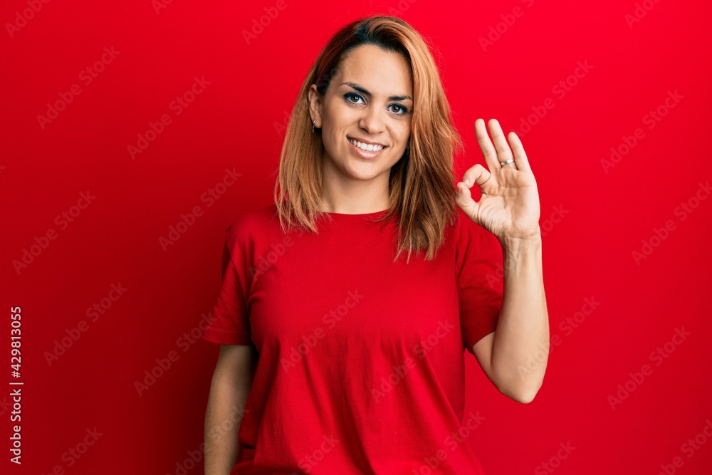 Hispanic young woman wearing casual red t shirt smiling positive doing ok sign with hand and fingers. successful expression. Hispanic young woman wearing casual red t shirt smiling positive doing ok sign with hand and fingers. successful expression.