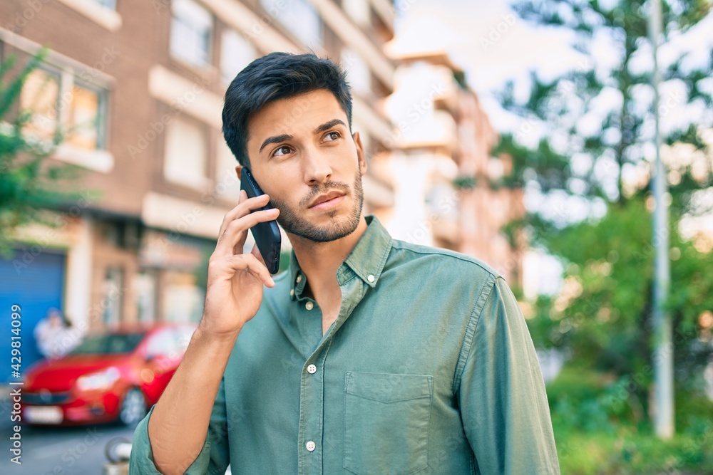 Young latin man with serious expression talking on the smartphone walking at the city. Young latin man with serious expression talking on the smartphone walking at the city.