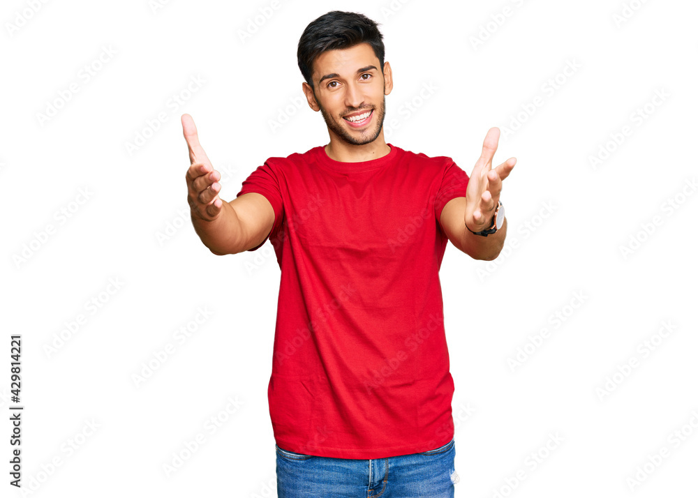 Young handsome man wearing casual red tshirt looking at the camera smiling with open arms for hug. cheerful expression embracing happiness. Young handsome man wearing casual red tshirt looking at the camera smiling with open arms for hug. cheerful expression embracing happiness.